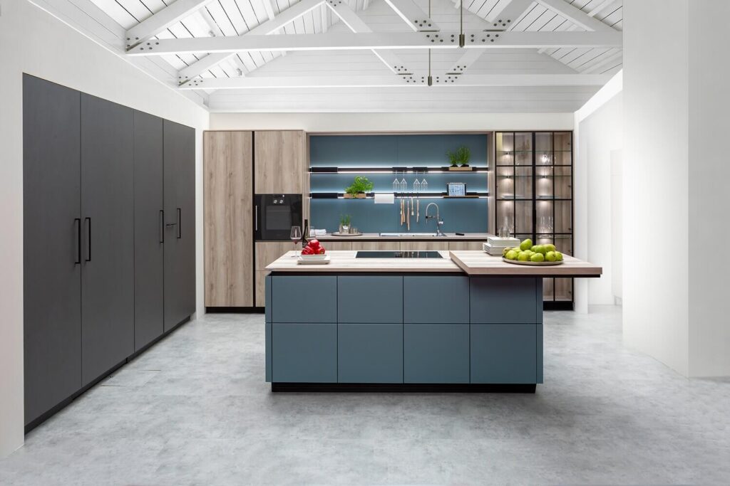 Moderne Ballerina Küche mit blauen Fronten, Holzdetails und offener Regalbeleuchtung unter weißem Dachgebälk.